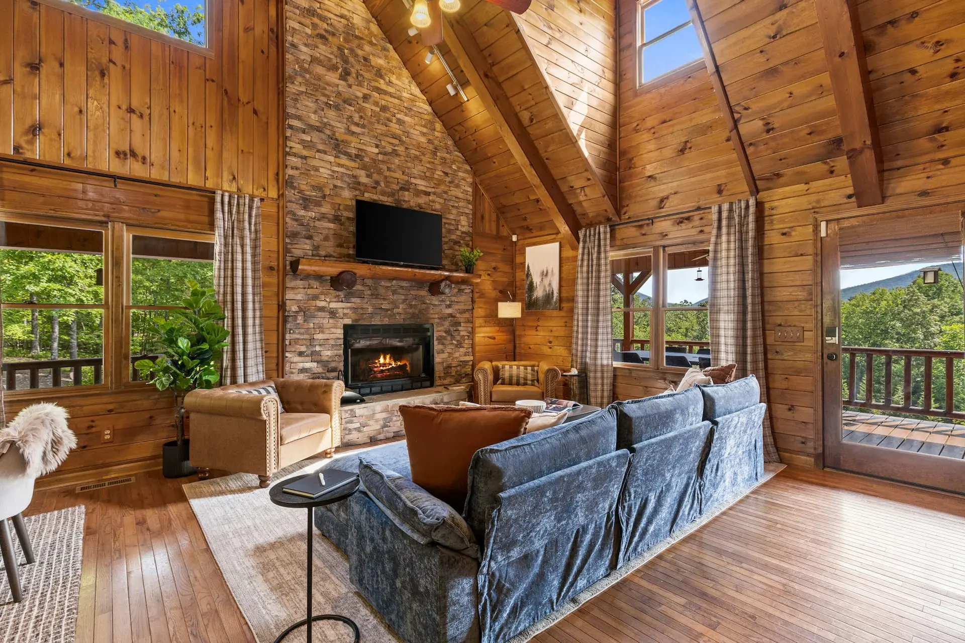 Cozy up by the stone fireplace in this stunning cabin living room with vaulted ceilings, warm wood interiors, and beautiful views just steps from the deck.