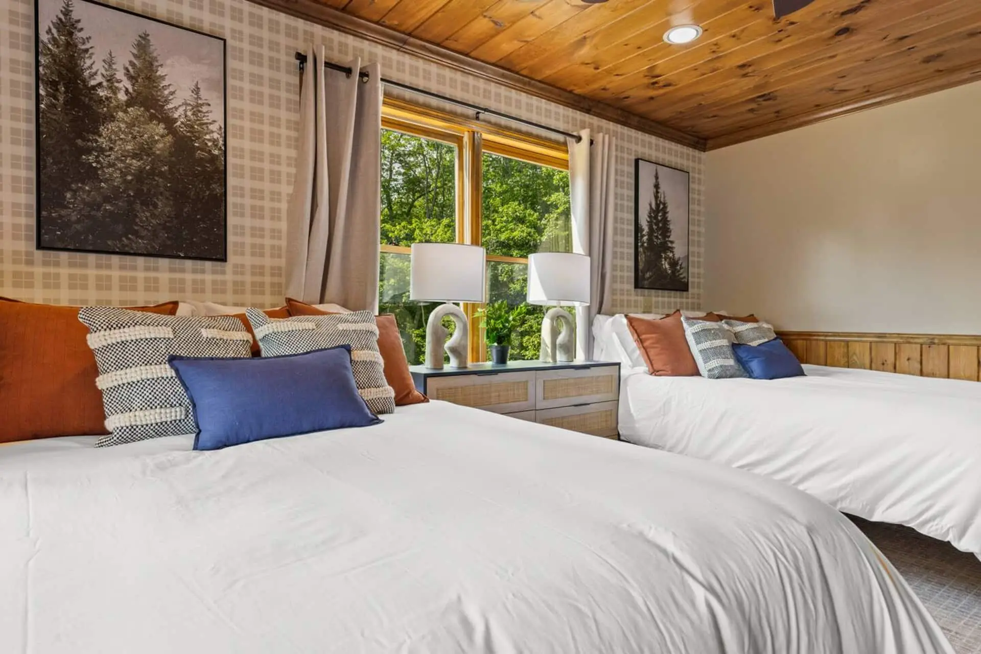 This inviting bedroom features two comfortable queen beds, warm wood accents, and a large window overlooking the trees. Soft lighting and cozy décor create a relaxing space perfect for families or friends traveling together.