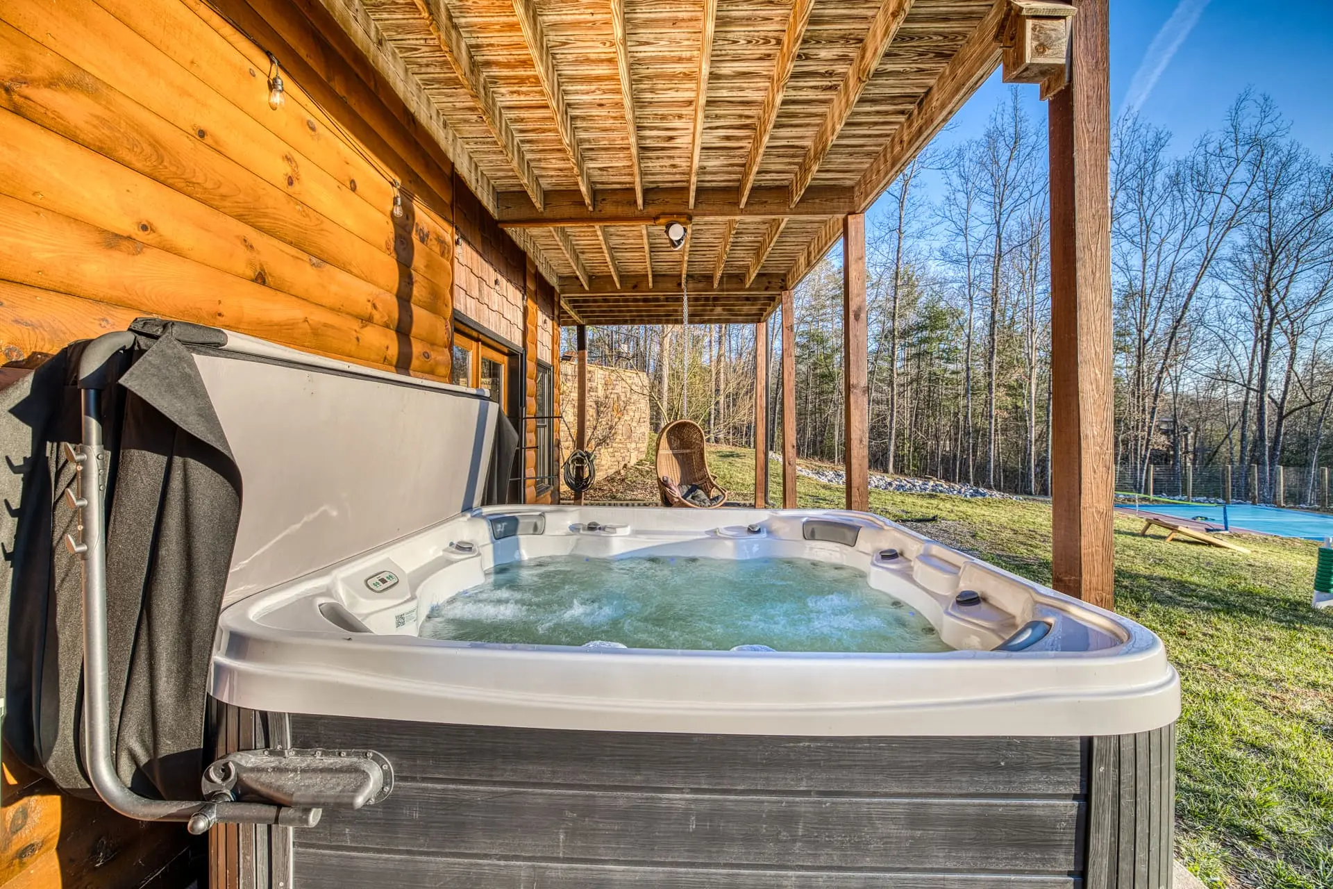 Covered hot tub with forest views and egg chair at rustic cabin retreat.